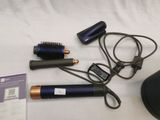 une photo montrant un sèche-cheveux, une brosse et d'autres objets disposés sur un lit