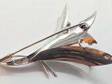 a silver brooch with a fish on it on a white surface