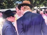 a man in a hat and sunglasses talking to another man in a suit