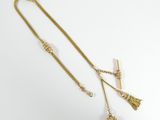 a gold necklace with a tassel on a white background