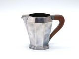 a silver pitcher with a wooden handle on a white surface
