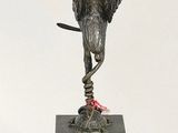 bronze statue of a bird on a pedestal with a red ribbon