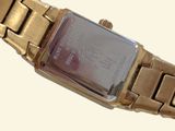 a gold wrist watch with a red face on a white background