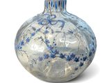 a glass vase with blue flowers in it on a white surface