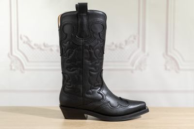 un gros plan sur une paire de bottes de cow-boy noires posées sur une table en bois