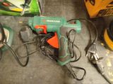 a green and orange corded drill on the floor