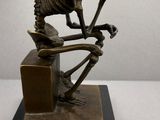 statue of a skeleton sitting on a desk with a pipe in its mouth