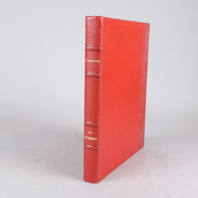 un vieux livre rouge posé sur une table à côté d'un mur blanc