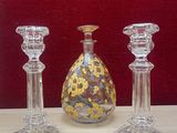 three glass candlesticks on a table with a vase in the background