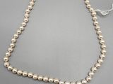 un collier de perles blanches muni d'un fermoir en or sur fond gris