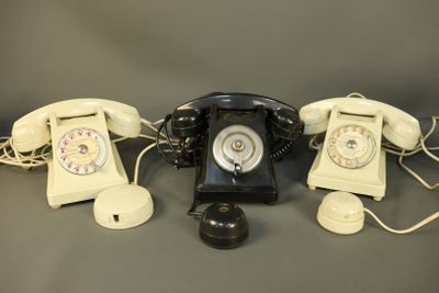 three old fashioned telephones are lined up on a gray surface