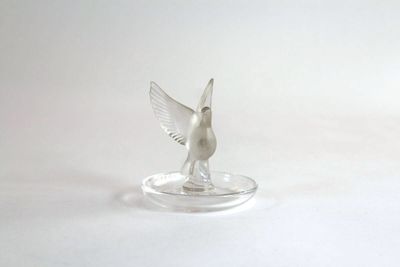 a small silver bird on a clear plate on a white surface