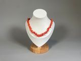 collier composé de perles de corail rouge montées sur un support en bois, sur fond gris