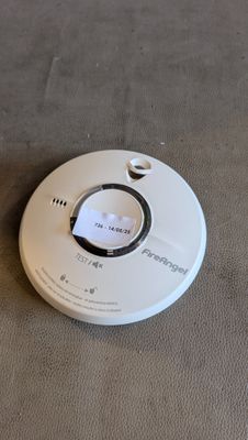 un détecteur de fumée blanc posé par terre à côté d'une télécommande
