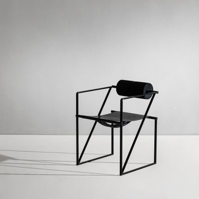 une chaise noire posée sur un sol blanc, près d'un mur