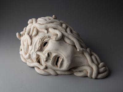 sculpture représentant une tête d'homme avec une tête de serpent au milieu