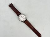 gros plan d'une montre sur une surface blanche avec un bracelet marron