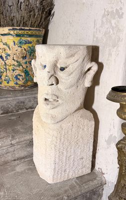 une statue représentant la tête d'un homme, posée sur une étagère à côté d'un vase