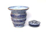 un vase bleu avec un couvercle posé à côté, sur une surface blanche