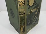 an old book sitting on top of a white table next to a clock
