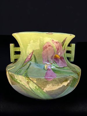 un vase vert orné de fleurs violettes, posé sur un fond noir