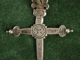 une croix en argent sur du velours vert, surmontée de perles en argent