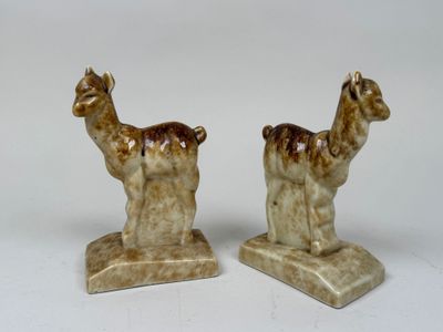 pair of ceramic figurines of llamas on stand on white background