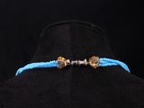 a gold and blue beaded bracelet with two charms on a black mannequin