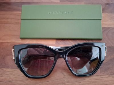 des lunettes de soleil et leur étui posés sur une table en bois, à côté d'une boîte verte