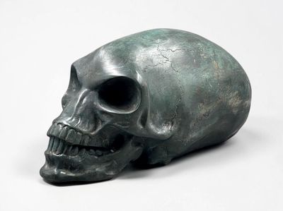 a bronze skull sitting on a white surface