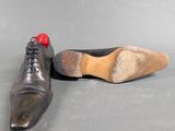 pair of black leather shoes with red rubber soles on grey surface
