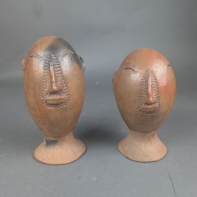 deux vases ornés de visages, posés sur un fond gris