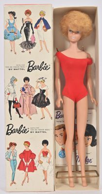 une poupée Barbie dans une boîte, avec plein de vêtements dessus