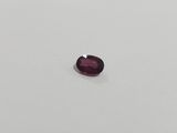 an oval cut purple garnet stone on a white surface