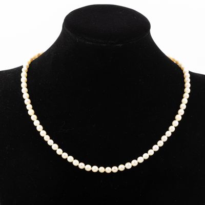 un collier de perles blanches autour du cou d'un mannequin, muni d'un fermoir en or