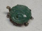 une image représentant une broche en forme de tortue en jade vert posée sur une surface blanche