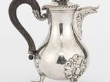 une cafetière ancienne en argent posée sur un support, sur fond blanc