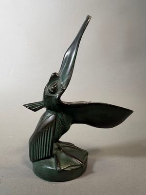 statue en bronze représentant un oiseau au long bec, posée sur une surface blanche