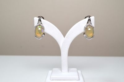 une paire de boucles d'oreilles en oplite jaune et diamants, posée sur un socle blanc