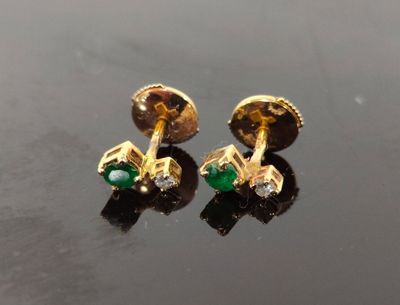 paire de boucles d'oreilles dorées et vertes, ornées de diamants, sur un fond noir