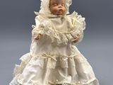 an antique porcelain doll of a baby wearing a white dress and bonnet