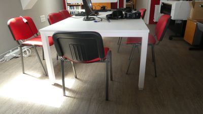 une table blanche avec des chaises rouges et un ordinateur posé dessus