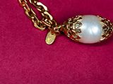 a close up of a gold necklace with a pearl on it