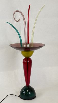 a red and green vase on a stand with a wire