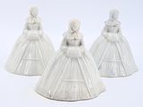 three white ceramic figurines of women dressed in dresses