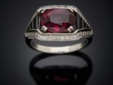 a close up of a ring with a ruby stone and diamonds