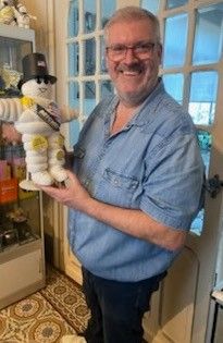 un homme souriant tenant une peluche devant une vitrine en verre