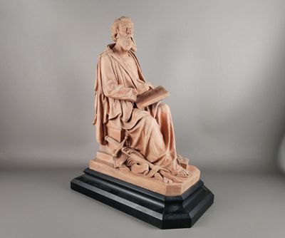 une statue représentant un homme assis sur une chaise en train de lire un livre