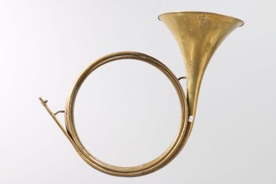 an antique brass french horn on a stand against a white background