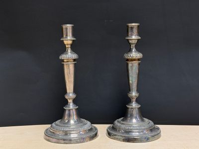 une paire de bougeoirs en argent posés sur une table en bois devant un mur noir